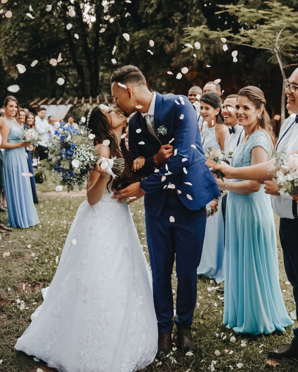 A white wedding welcome sign on an easel, the printed hashtag visible across the top, a small bouquet of blush flowers at its base.